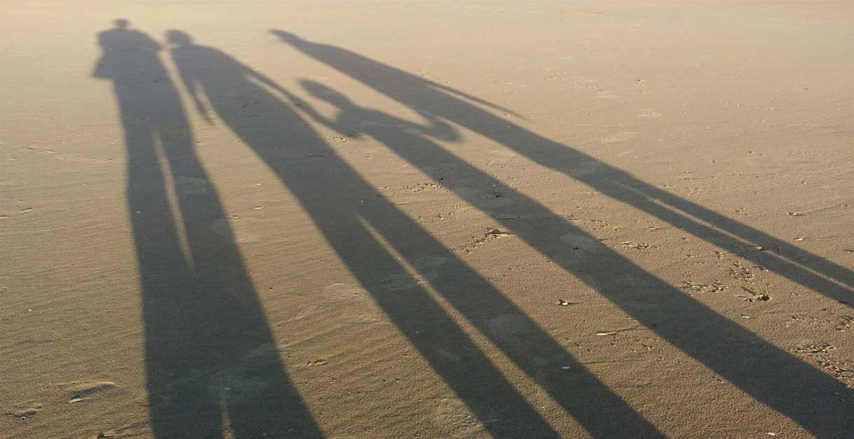 foto di una spiaggia su cui si proietta l'ombra di una famiglia